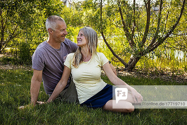 Outdoor portrait of a mature married couple sitting on the grass in a park looking at each other; Edmonton  Alberta  Canada