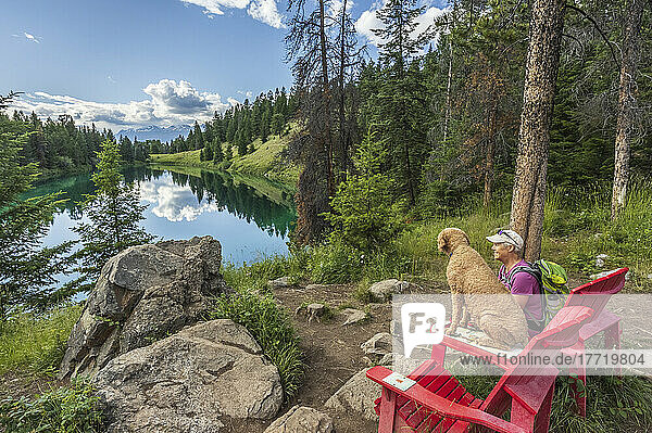 Senior woman and her dog enjoy the two red adirondack chairs at Valley of the Five Lakes in Jasper National Park; Alberta  Canada