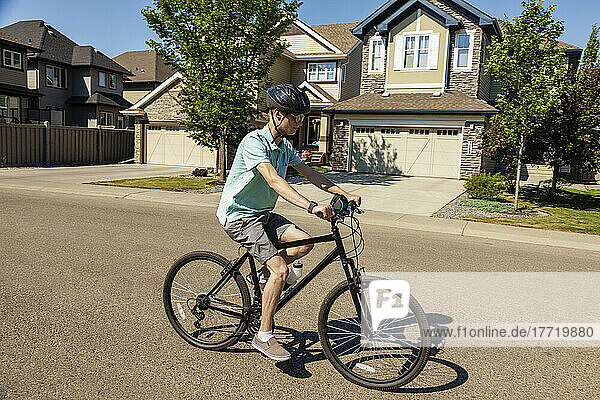 Junger Mann fährt mit dem Fahrrad eine Wohnstraße entlang; Edmonton  Alberta  Kanada
