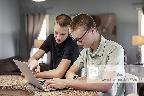 Junger Mann benutzt zu Hause einen Laptop  sein Bruder hilft ihm dabei; Edmonton  Alberta  Kanada