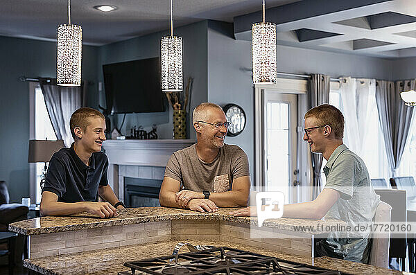 Father and two sons sit at the kitchen island at home talking together; Edmonton  Alberta  Canada