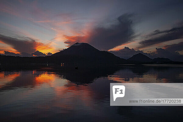 Dramatische Schönheit des Spiegelbilds des Vulkans Tavurvur und glühende Wolken bei Sonnenaufgang im ruhigen Ozeanwasser; Neubritannien  Papua-Neuguinea