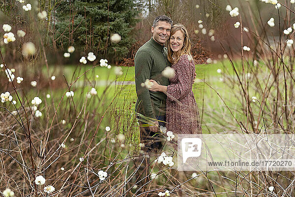 Mid adult couple stand outdoors in a park in an affectionate embrace with blossoms in the foreground; Aldergrove  British Columbia  Canada