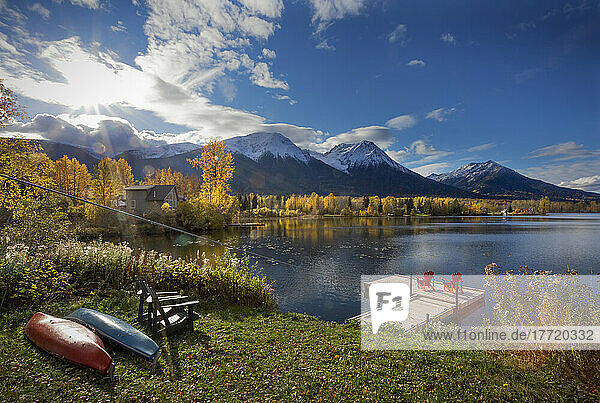 Two red chairs on a deck on tranquil Lake Kathlyn surrounded by autumn coloured trees and snow-capped Coast Mountains  viewed from Lakedrop Inn  Watson's Landing  BC  Canada; Smithers  British Columbia  Canada