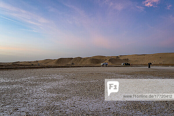 Tourists and vehicles on a desert landscape at sunset; Abu Dhabi  United Arab Emirates