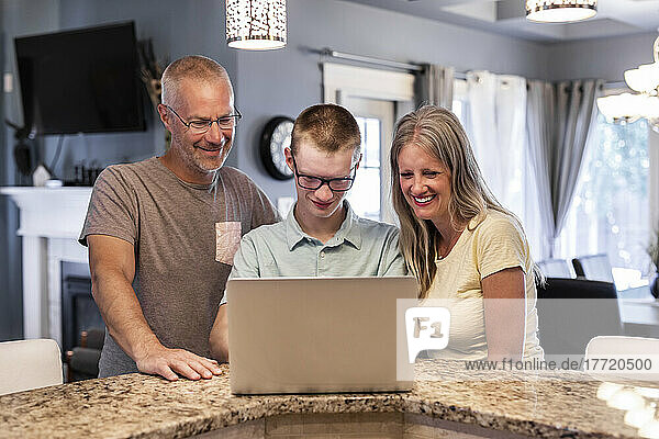 Junger Mann  der zu Hause einen Laptop benutzt  während seine Eltern zusehen; Edmonton  Alberta  Kanada