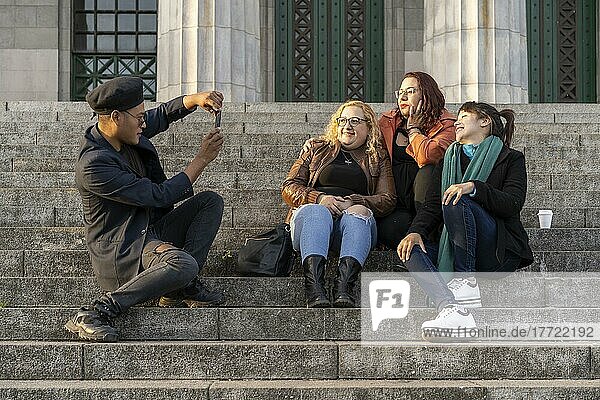 Eine multiethnische Gruppe von Freunden sitzt auf einer Treppe und unterhält sich  lacht und macht Fotos