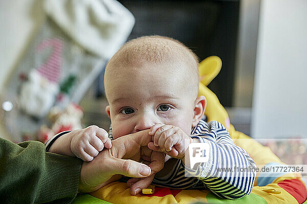 Nahaufnahme eines sechs Monate alten Babys  das sich am Finger seiner Mutter festhält und in die Kamera schaut
