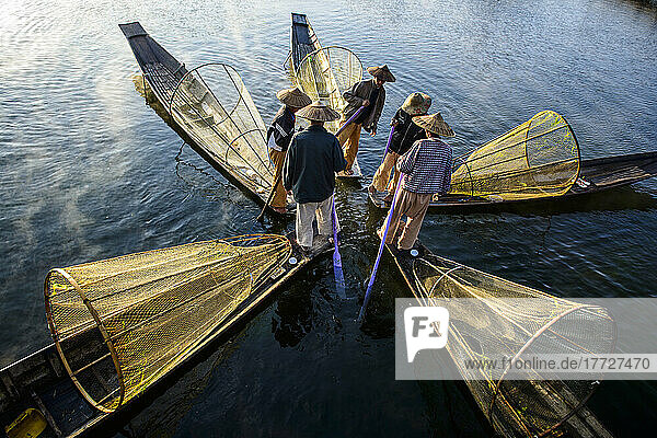 Five fishermen on traditional boats with conical fishing nets.