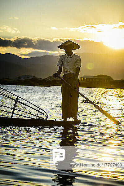 A fisherman standing on his boat fishing on Lake Inle at dusk.