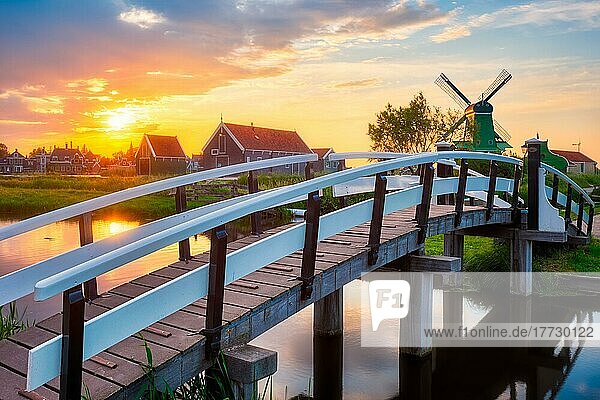 Ländliche Szene in den Niederlanden  Brücke über den Kanal und Windmühlen am berühmten Touristenort Zaanse Schans in Holland bei Sonnenuntergang mit dramatischem Himmel. Zaandam  Niederlande  Europa