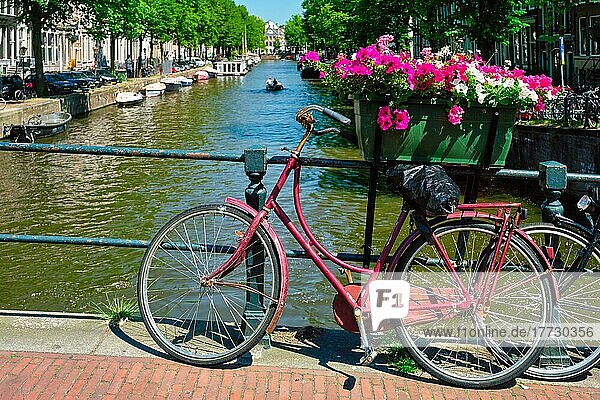 Typische Amsterdamer Ansicht  Amsterdamer Gracht mit Booten und geparkten Fahrrädern auf einer Brücke mit Blumen. Amsterdam  Niederlande  Europa