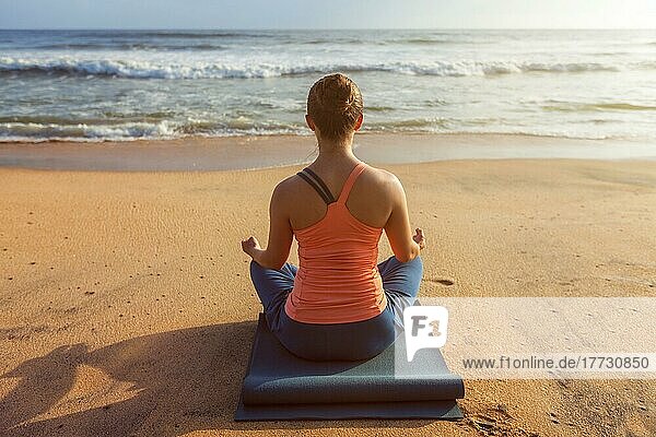 Frau macht Yoga  meditiert und entspannt in Padmasana Lotus Pose im Freien am tropischen Strand bei Sonnenuntergang