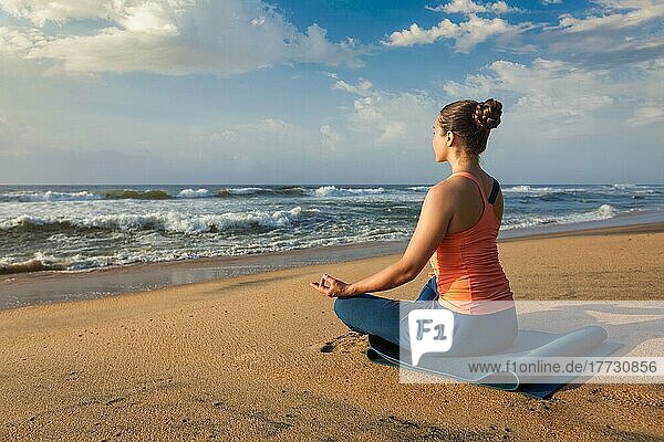 Woman doing yoga  meditating and relaxing in Padmasana Lotus Pose outdoors at tropical beach on sunset
