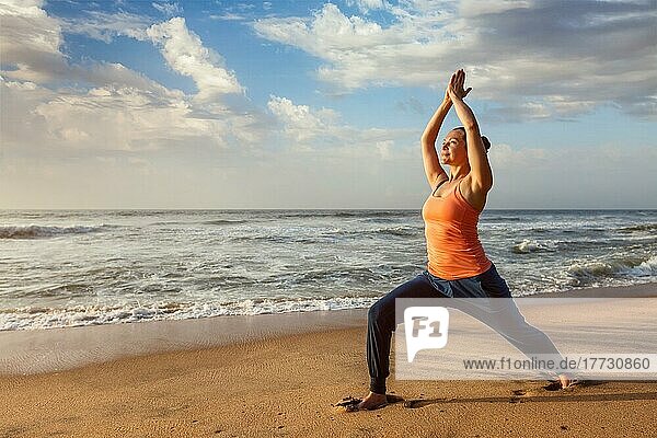 Frau macht Hatha Yoga Asana Virabhadrasana 1 Warrior Pose im Freien am Strand bei Sonnenuntergang. Kerala  Indien  Asien