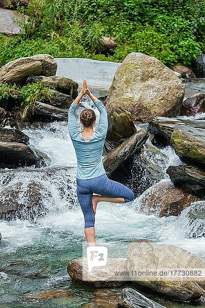 Frau in Hatha-Yoga-Balance-Yoga-Asana Vrikshasana Baumpose am Wasserfall im Freien