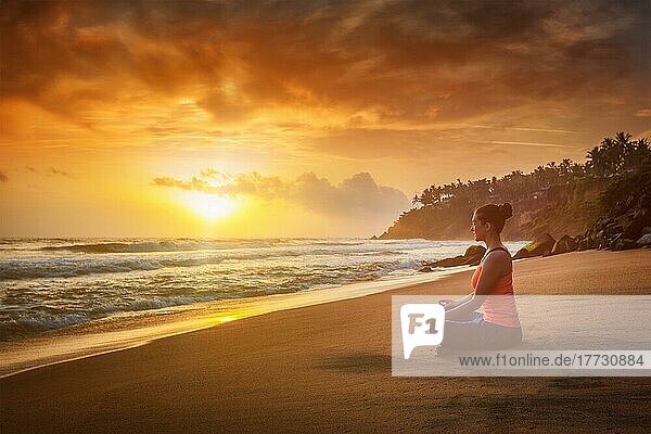 Junge sportliche  fitte Frau macht Yoga  meditiert und entspannt sich in Padmasana Lotus Pose) mit Kinn Mudra im Freien am tropischen Strand bei Sonnenuntergang