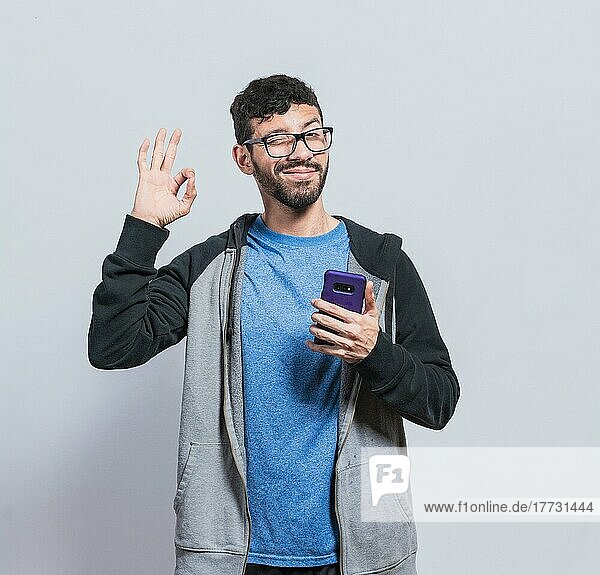 Angenehme Person  die ein Handy hält und zwinkert  lächelnder Junge mit Handy  der ein Ok-Zeichen macht  Konzept einer positiven Person mit Handy  die ihre Finger zu einem Ok-Zeichen schließt