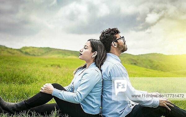 Ein Paar sitzt mit dem Rücken zueinander im Gras  ein Hochzeitspaar auf dem Feld sitzt mit dem Rücken zueinander und schaut in die Kamera