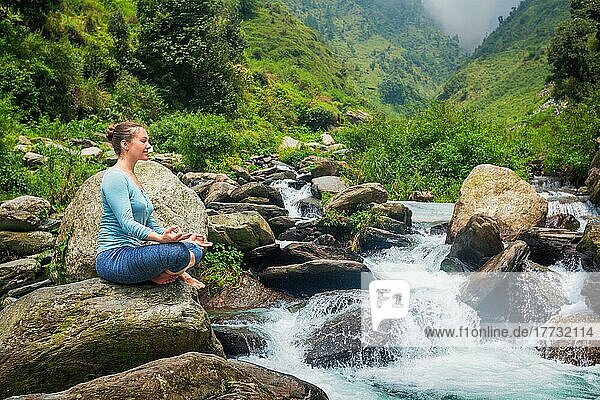 Frau in Hatha Yoga Asana Padmasana im Freien an einem tropischen Wasserfall