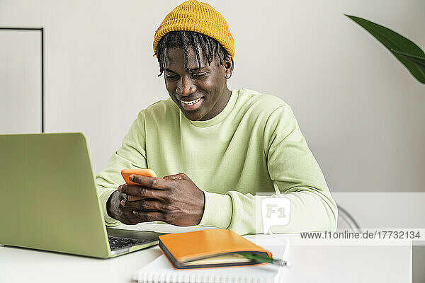 Smiling freelancer using smart phone at home office