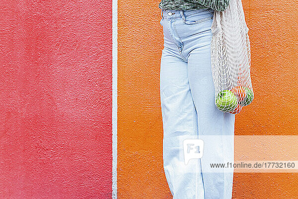 Woman with bag of fruits standing in front of red and orange wall