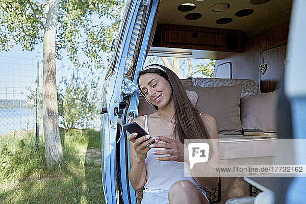 Lächelnde Frau benutzt Smartphone im Eingang ihres Wohnmobils