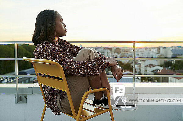Junge Frau sitzt mit geschlossenen Augen auf einem Stuhl auf dem Balkon