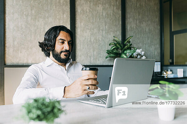 Businessman with coffee up using laptop at office