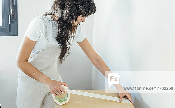 Woman with adhesive tape packing cardboard box at home