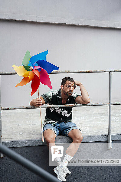 Bored man holding pinwheel toy sitting near railing