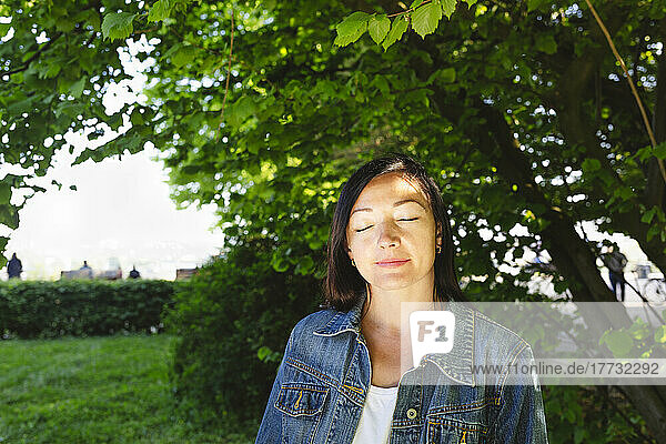 Woman wearing denim jacket with eyes closed in park