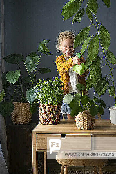 Girl with spray bottle watering potted plants at home