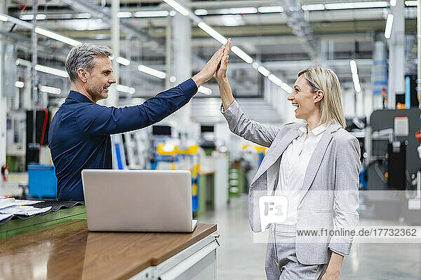 Happy businessman and businesswoman high fiving in factory
