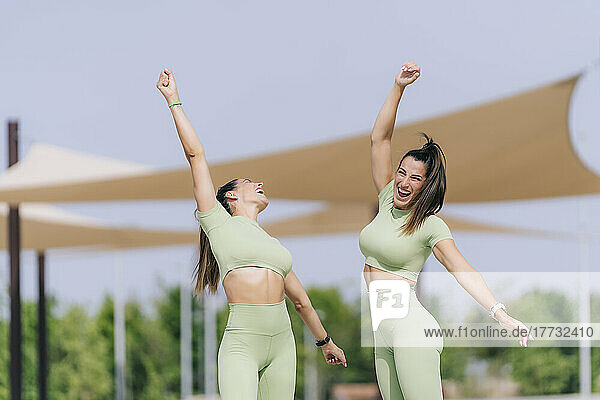 Cheerful twin sisters with hands raised enjoying sunny day