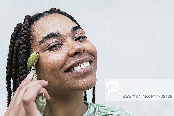 Happy young woman using jade roller against white background