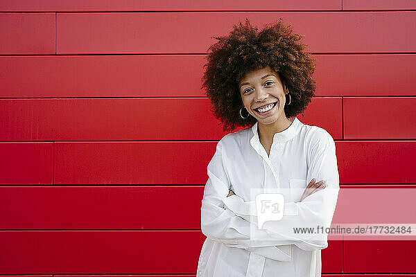 Smiling Afro woman standing with arms crossed in front of red wall
