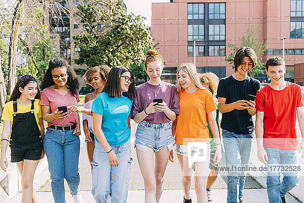 Lächelnde  gemischtrassige Freunde  die gemeinsam mit dem Smartphone spazieren gehen