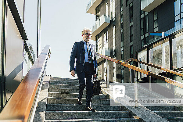 Senior businessman with briefcase walking down stairs on sunny day