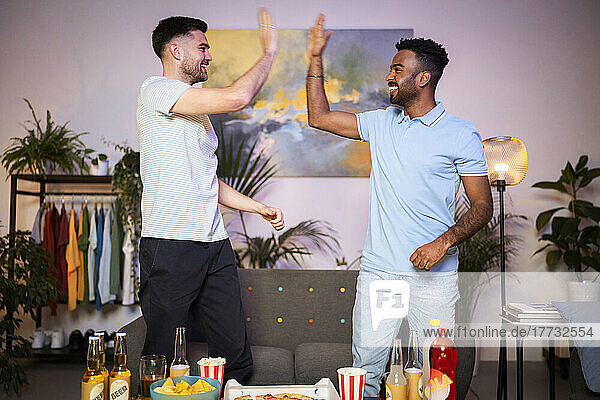 Happy young men giving high-five to each other standing in living room at home