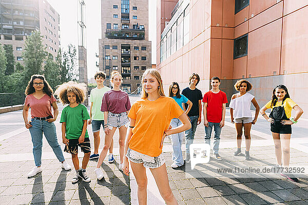 Smiling blond girl standing with hands on hip in front of friends