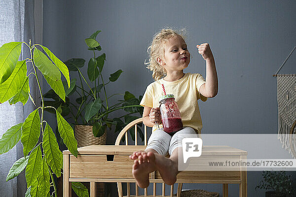 Girl drinking healthy fruit smoothie flexing muscles at home