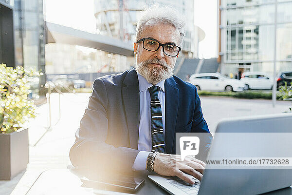 Senior businessman sitting with laptop outdoors
