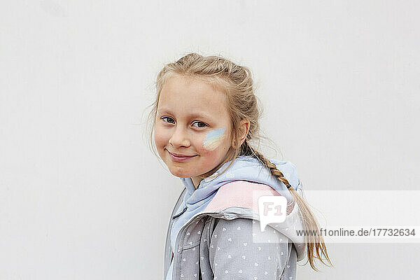 Smiling girl with Ukrainian flag painted on cheek against white background