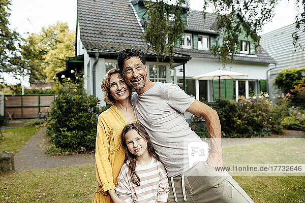 Happy parents with daughter standing in front of house