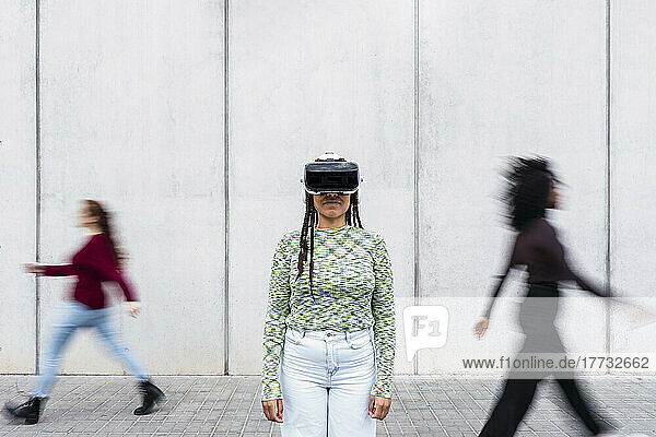 Young woman wearing virtual reality simulator standing in front of wall