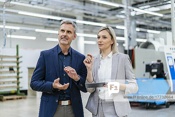 Businesswoman with digital tablet and businessman talking in factory