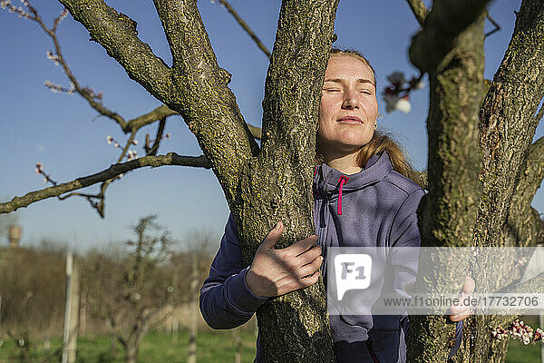 Mature woman with eyes closed hugging tree on sunny day