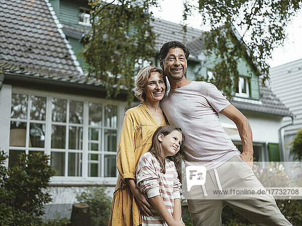 Happy parents with daughter standing in front of house