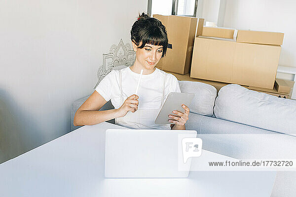 Smiling woman using tablet PC sitting with laptop at table